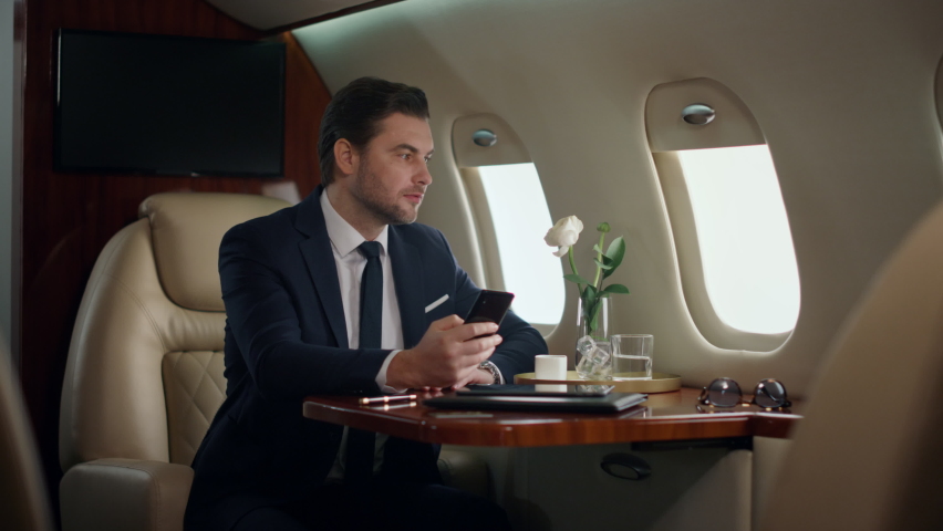 European businessman typing phone on airplane trip. Confident manager resting drinking coffee in luxury jet. Successful man texting surfing internet in suit. Happy gentleman check email use smartphone Royalty-Free Stock Footage #1091495211