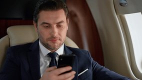 Handsome entrepreneur using smartphone in plane closeup. Successful ceo travel business class in suit. Focused elegant man scrolling checking email. Serious manager working analyzing stock market. - Powered by Shutterstock - Get 15% off with code: PIKWIZARD15