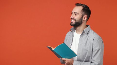 Happy fashionable swanky smiling young brunet man 20s years old wears blue shirt looking aside writing down in exercise book notebook diary notes isolated on plain orange background studio portrait