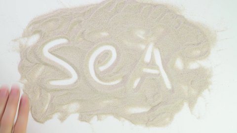 sea text. Top view draw on the sand. Caucasian hands write text in beige sand. Vacation and travel. Beach on vacation. Sand painting. Creativity from natural materials.