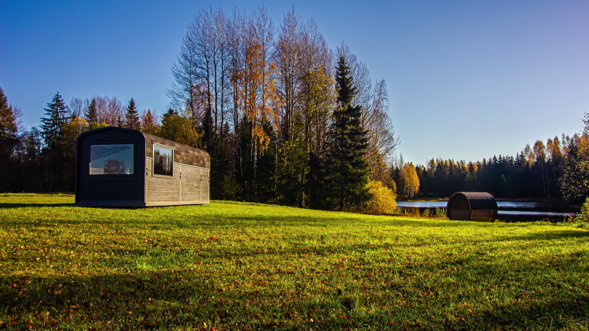 Beautiful timelapse shot of autumnal landscape surrounding a wooden cabin and a barrel sauna by the side of the lake throughout the daytime. Forest in the background.