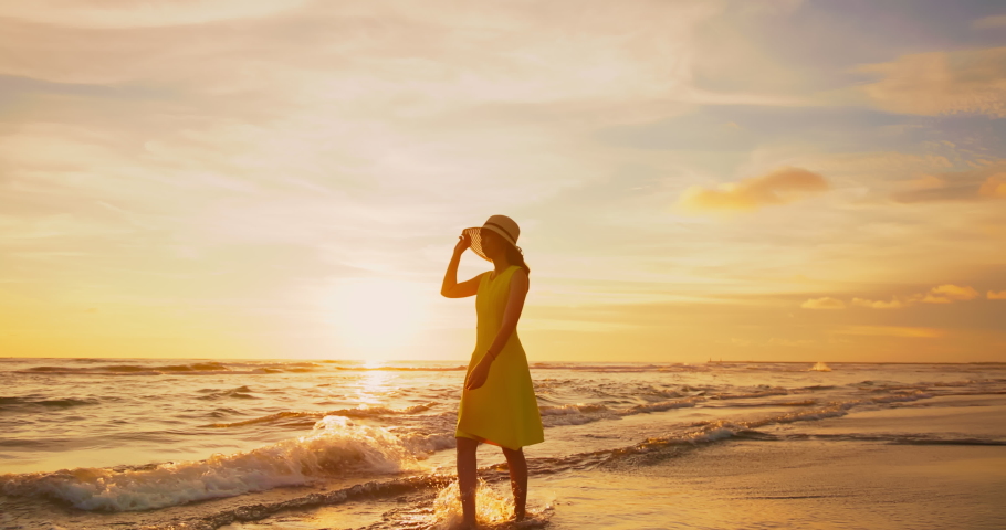 Slow motion side view of asian woman wearing beautiful yellow dress walking by beach at golden sunset - Female tourist on summer vacation | Shutterstock HD Video #1091502505