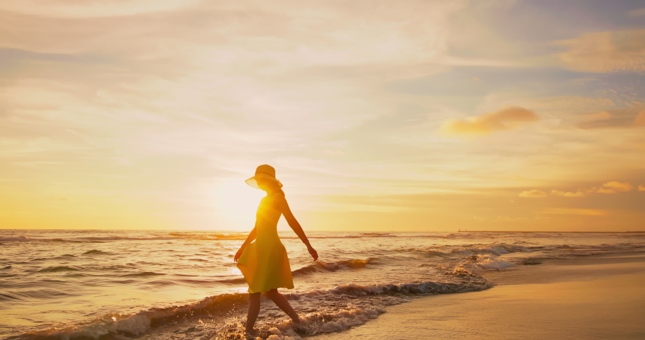 Slow motion side view of asian woman wearing beautiful yellow dress walking by beach at golden sunset - Female tourist on summer vacation | Shutterstock HD Video #1091502505