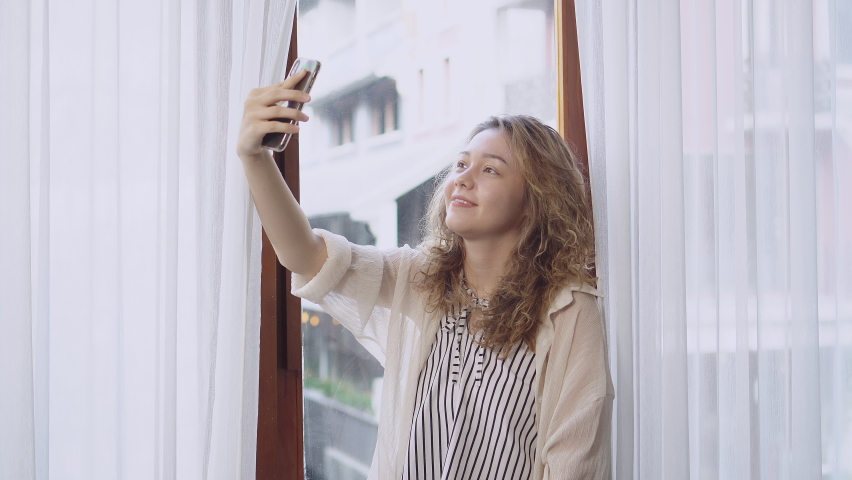 happy young asian woman dancing slow and enjoying music alone near window curtain. woman relax with activity at home in holiday