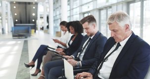 Youll find motivation online. 4k video footage of a group of businesspeople using digital devices while sitting in a line.