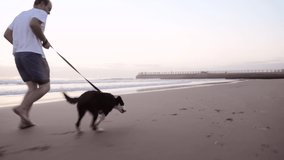 4k video footage of a man going for a run with his dog on the beach at sunset