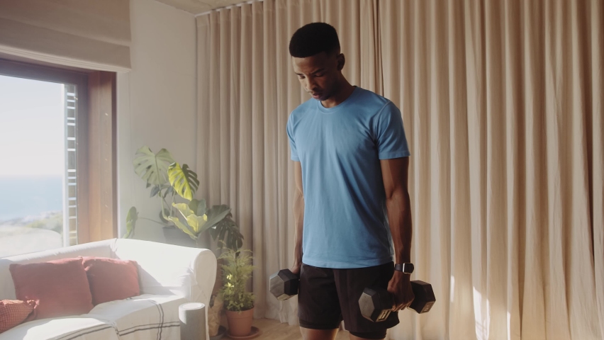 Young African American black male working out in living room at home doing a bicep curl with heavy dumbbell weights. Keeping fit and healthy with strength training Royalty-Free Stock Footage #1091510861