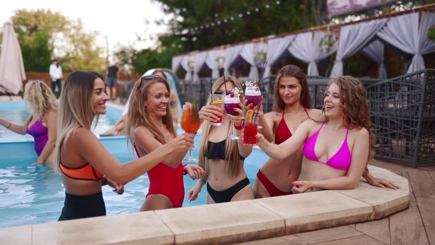 Girls in bikini have pool party with cocktails in swimming pool. Women relaxing clinking glasses with drinks at luxury resort. Female friends in red swimwear dancing, clubbing in a water. Slow motion. Royalty-Free Stock Footage #1091511155