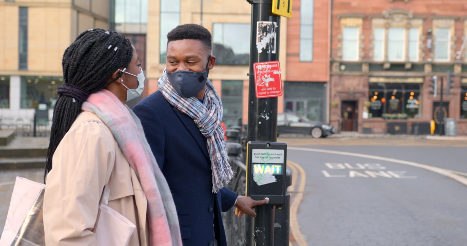 Couple wearing face coverings chatting, about to cross main road in town centre