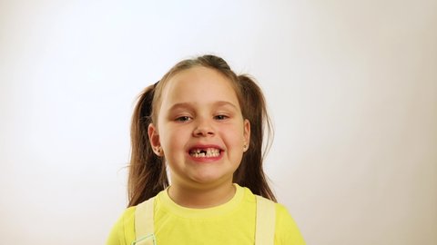 Little funny girl wide smiling with gap in mouth from fallen tooth and diligently showing all teeth closeup, white background. Joyful toothless child. Concept of healthy teeth and beautiful smile.
