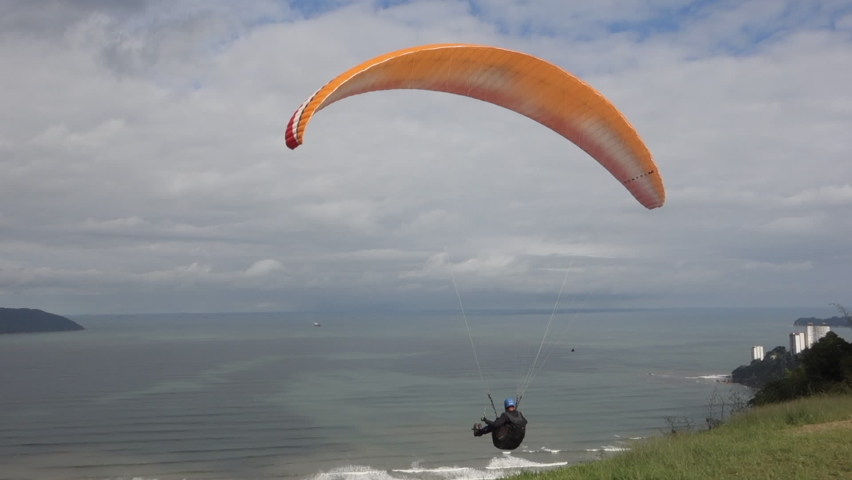 Paraglide pilot launches from grass ramp high above cloudy beach Royalty-Free Stock Footage #1091517715