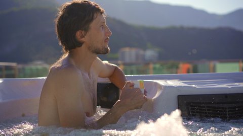 A young man relaxes in the hot tub on a rooftop with a view on mountains