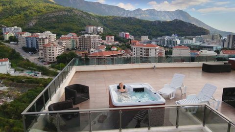 Slowmotion video. Aerial shot of a young woman relaxes in the hot tub on a rooftop
