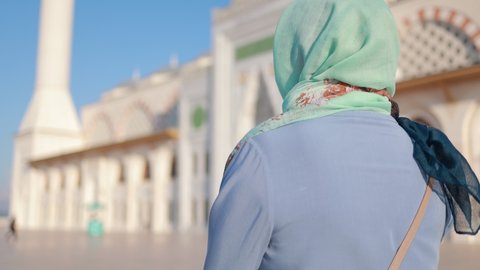 A woman in a headscarf walks in a mosque on a sunny summer day