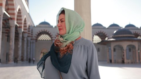 A woman in a headscarf walks in a mosque on a sunny summer day