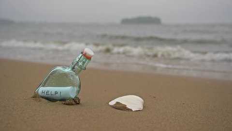 Bottle on beach with message on paper inside in rainy day in slow motion