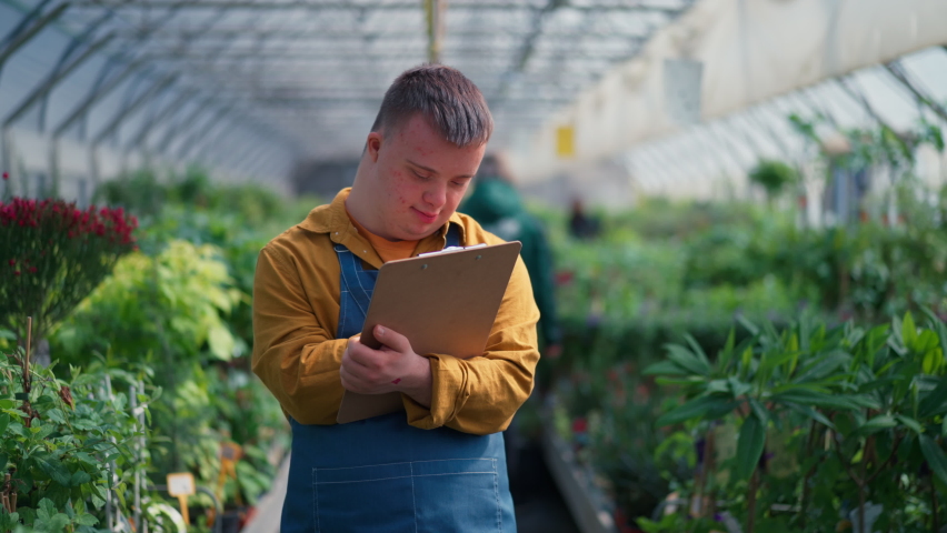 Young man working in garden centre, holidng clipboard and checking plants.