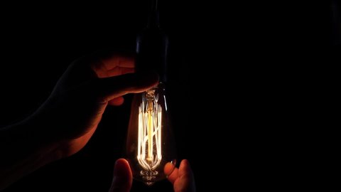 Retro design of light bulbs. A man's hand twists in an incandescent light bulb and it starts to glow. The electrician changes the light bulb.