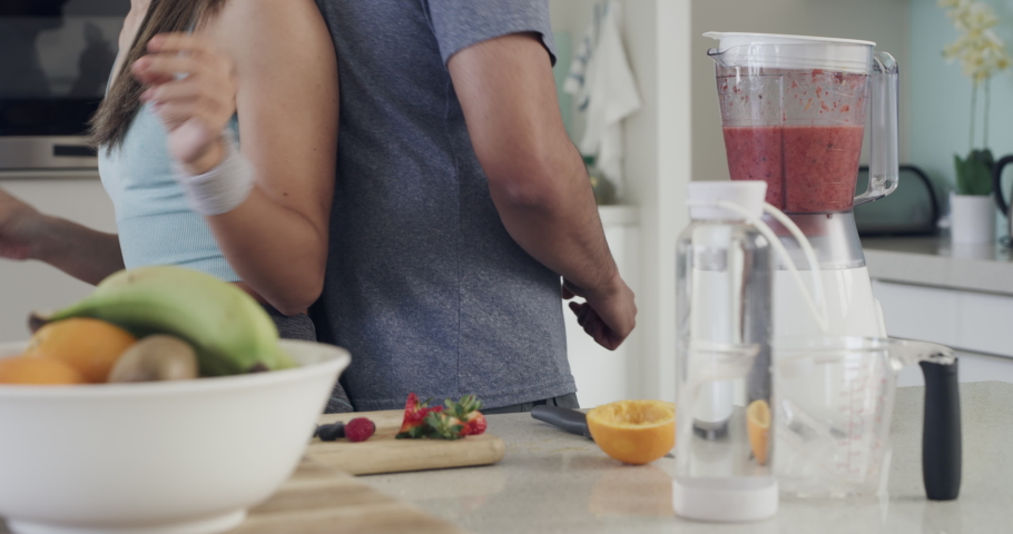 Two fit young athletic people having fun while singing in a kitchen and making smoothies. Diverse couple being playful while making health shakes with fresh fruit and dancing in a bright apartment Royalty-Free Stock Footage #1091532693