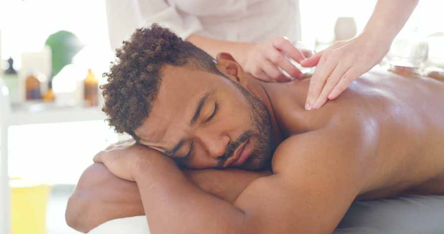 Young relaxed man enjoying relaxing and therapeutic back massage treatment with vacuum cups in a spa. Beauty therapist treating muscle pain with suction cupping therapy to remove body toxins Royalty-Free Stock Footage #1091532755