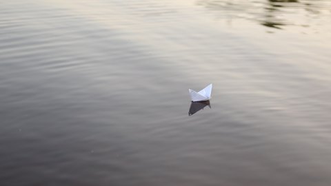 A paper boat is floating on the waves in the water at a beautiful sunset. Origami ship Sailing. The concept of a dream, future, childhood, freedom or hope. Slow motion. High quality FullHD footage.