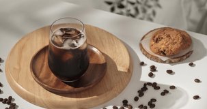 4k video, pouring creamy milk into a brewing iced coffee is served with cookies. Cold coffee drink glass with ice and cream milk on white table. in slow motion.