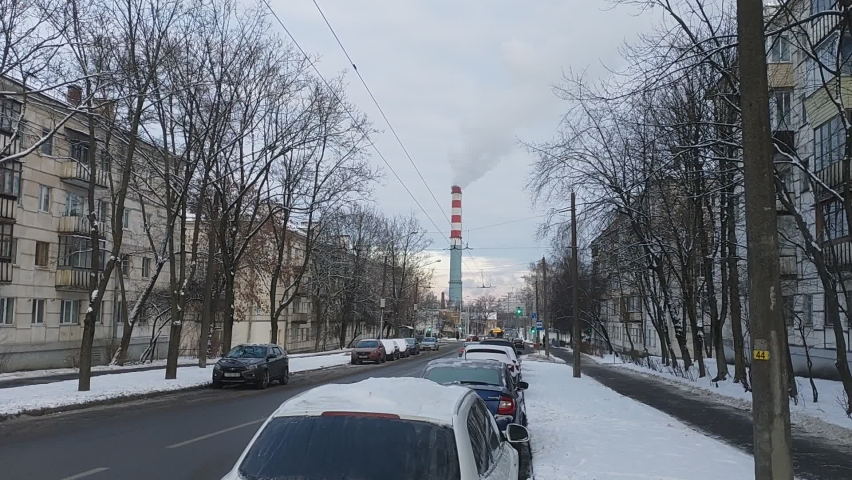 There is smoke coming from the chimney of the power plant. Cars drive through the streets of the city. After the snowfall, a snow cover has formed in the city