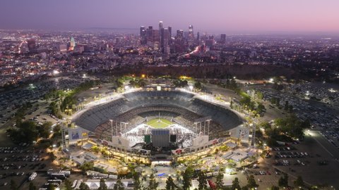 Crowd of people having fun during music festival on Dodgers Stadium illuminated at night 4K aerial. Los Angeles buildings in downtown at cinematic pink sunset. Dodgers Stadium, Los Angeles June 2022