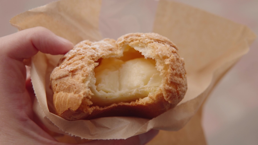 Profiterole with caramel cream in the hand of a person close-up, street food, delicious urban pastries.