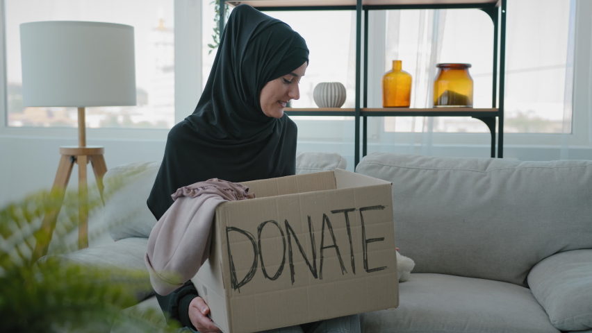 Arabian Islamic Muslim female in black hijab kind woman volunteer at home sitting on couch packing donations box with clothes and toys for kids putting teddy bear in parcel war donating volunteering Royalty-Free Stock Footage #1091540655