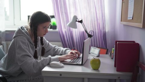 A student with glasses and pigtails is typing rapidly on a laptop keyboard.