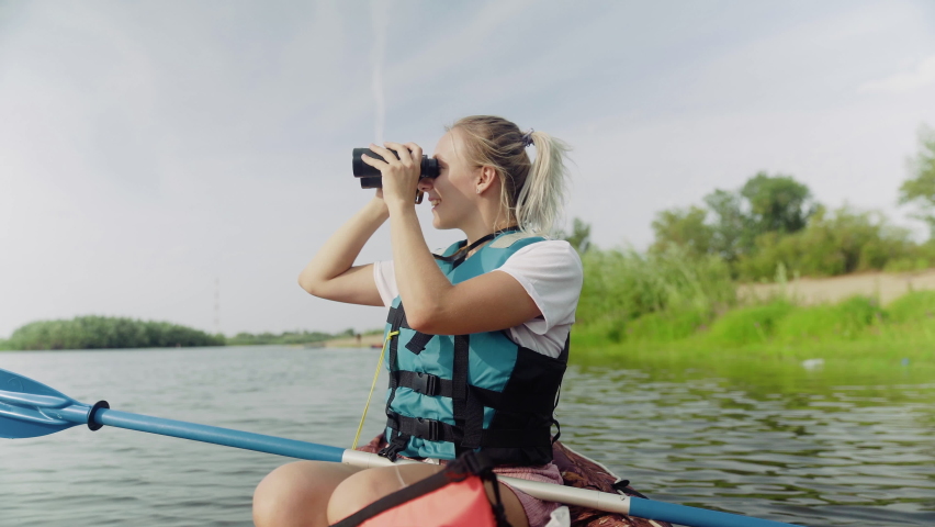 A young woman is kayaking on the river against a beautiful landscape and looking through binoculars. Travel. Tourism. | Shutterstock HD Video #1091550425