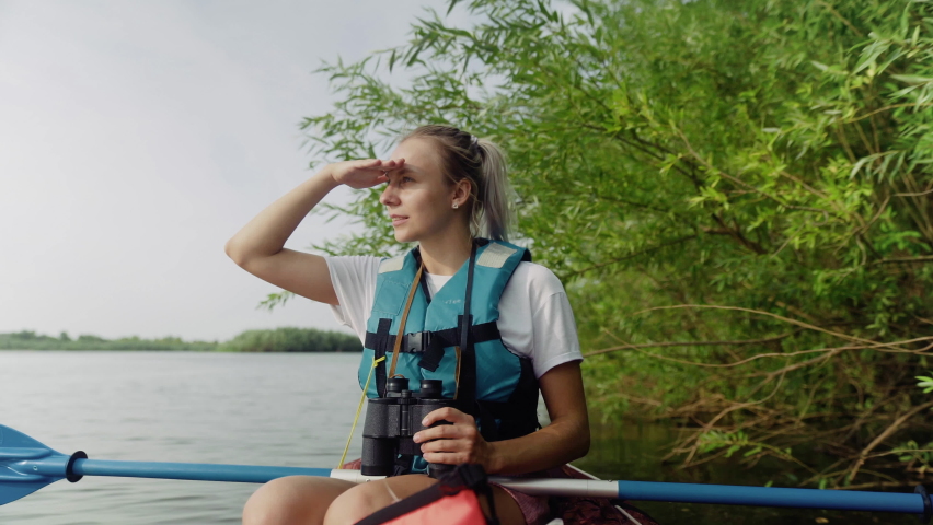 A young woman is kayaking on the river against a beautiful landscape and looking through binoculars. Travel. Tourism. | Shutterstock HD Video #1091550429