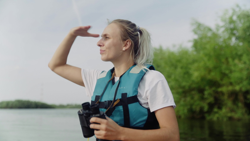 A young woman is kayaking on the river against a beautiful landscape and looking through binoculars. Travel. Tourism. | Shutterstock HD Video #1091550431