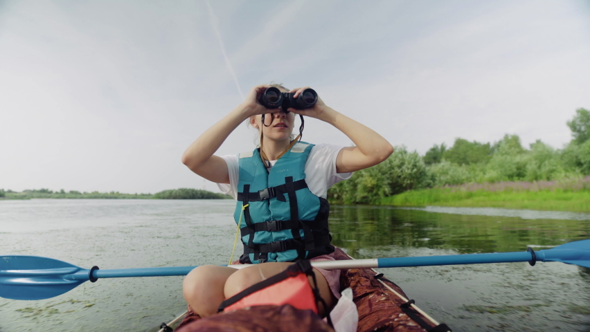 A young woman is kayaking on the river against a beautiful landscape and looking through binoculars. Travel. Tourism. | Shutterstock HD Video #1091550433