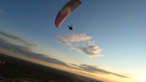 Dynamic aerial shot of paraglider flying along the river and against sunset sky 