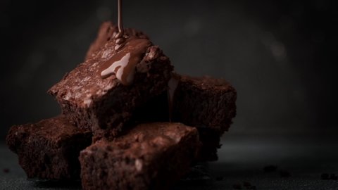 Pouring melted chocolate on cake biscuits in a slow motion. Brownies with chocolate icing on black background