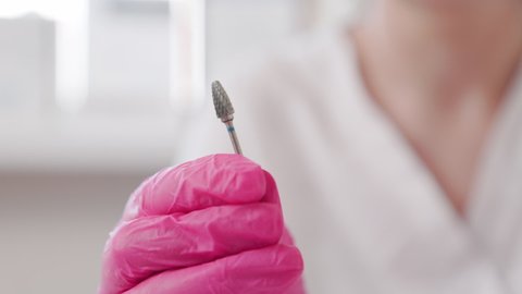 A cosmetologist in medical pink gloves shows a close-up of an abrasive nozzle for filing nails. Slow motion. The concept of manicure, pedicure and chiropody.