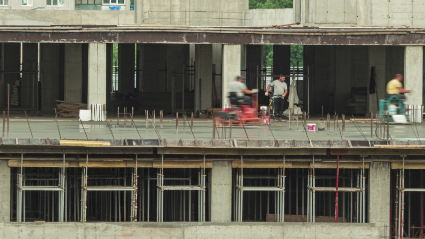 Workers at a construction site are smoothing and sanding a newly poured concrete floor with a mechanized screed. A timelapse of the construction of the indoor multi-level parking lot