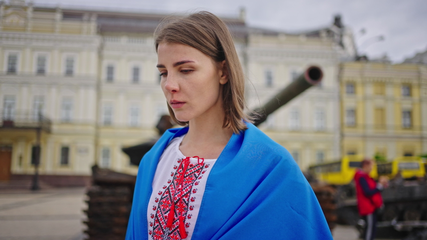 Sad woman puts palms in prayer gesture calling for peace in Ukraine. Patriotic lady covered with Ukrainian flag begs for help standing against tank in Kyiv closeup Royalty-Free Stock Footage #1091557873