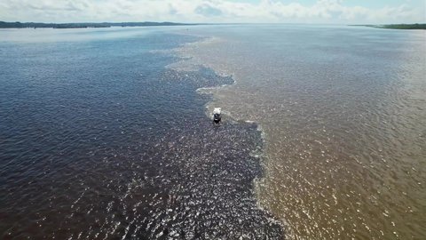 Boat sailing at Meeting of the Waters tourism landmark at Manaus Amazonas Brazil. Brown Amazon river side Black Negro River with two different colors. Amazon rainforest Brazil. Manaus Amazonas Brazil.
