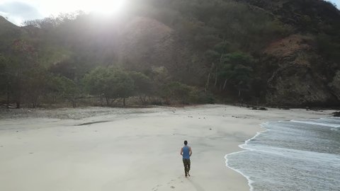 A man walking on an idyllic Koka Beach. Hidden gem of Flores, Indonesia. Couple is enjoying their romantic escape. Waves gently washing the shore. There are hills in the back. Adventure and discovery
