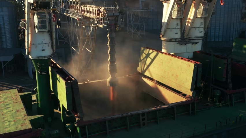 Aerial of wheat loading to bulker ship cargo hold at sea grain elevator in sea port. Wheat pouring from silo to bulk vessel via trunk at sea port terminal. Transportation of agricultural commodities. Royalty-Free Stock Footage #1091562217