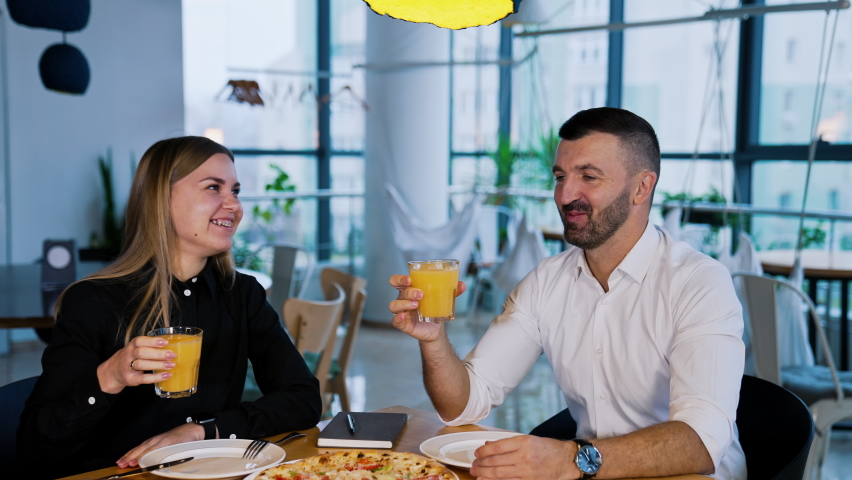 Happy smiling young people clink glasses with juice sitting at table. Company of friends came to have some pizza together. | Shutterstock HD Video #1091562619