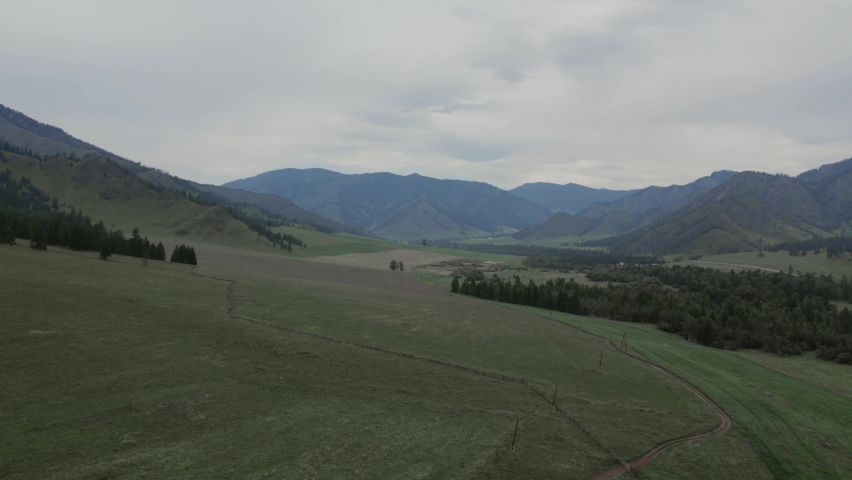 Rural fields and mountains under blue sky with white clouds in Altai, Siberia, Russia. Beautiful summer nature landscape at during daytime. Aerial view from a drone