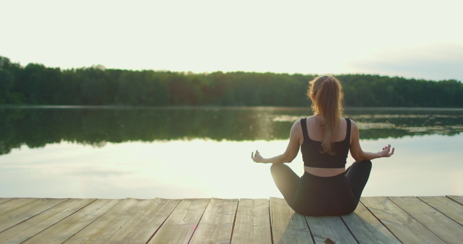 Back view of girl in the lotus position meditating on the shore of the lake | Shutterstock HD Video #1091563157