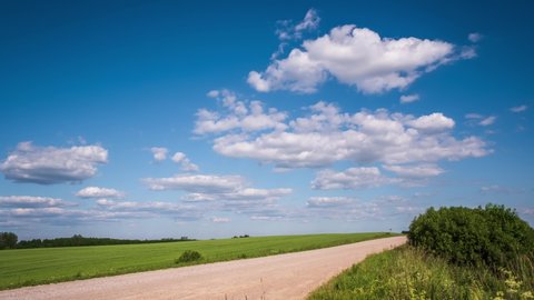 time lapse of sky background with tiny fluffy clouds in sunny day over forest with gravel road