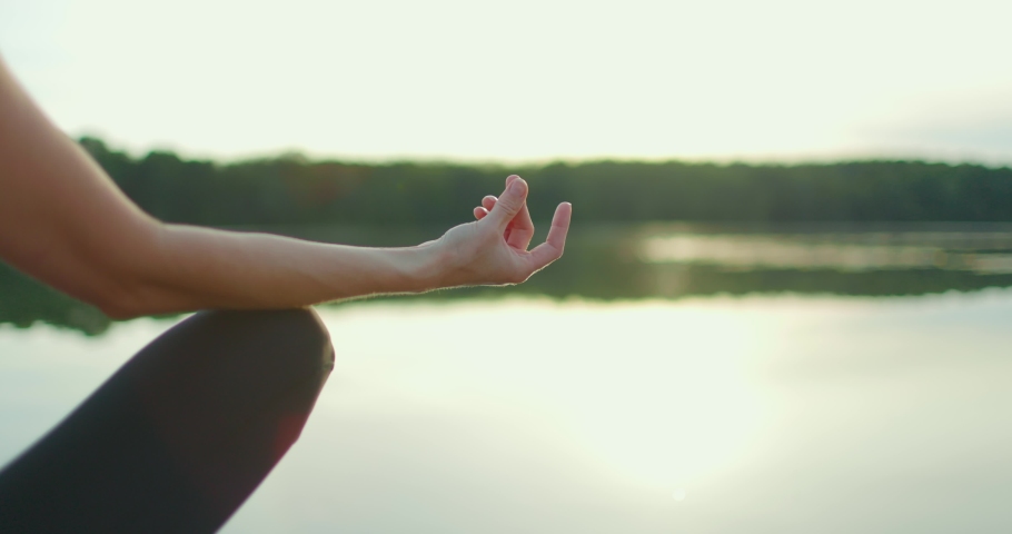 Young woman in sports clothes is sitting in lotus position and meditating on the shore of lake. Close-up | Shutterstock HD Video #1091568061