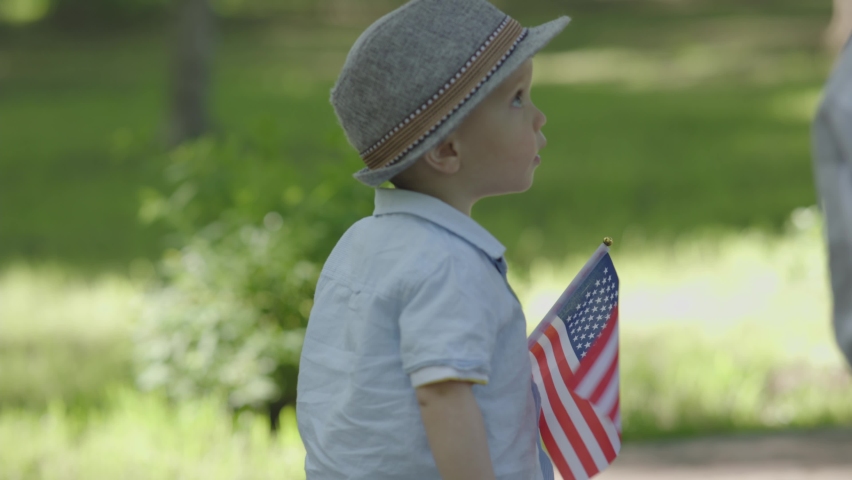 Baby child toddler walking city park holding national American flag Independence Day. concept of celebrating 4th July happy patriot USA citizen. Happy memorial Day or Veterans Day.  | Shutterstock HD Video #1091568245