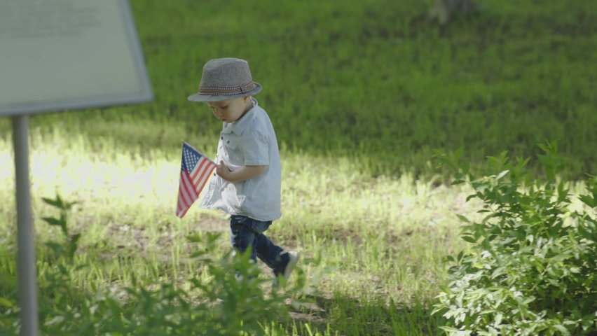 Baby child toddler walking city park holding national American flag Independence Day. concept of celebrating 4th July happy patriot USA citizen. Happy memorial Day or Veterans Day.  | Shutterstock HD Video #1091568253